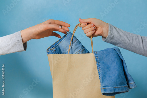 One hand of the child is passing a craft paper bag with blue jeans to the other hand. Concept of thrift stores, resale, second hand.