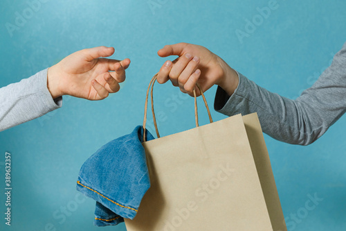 One hand of the child is passing a craft paper bag with blue jeans to the other hand. Concept of thrift stores, resale, second hand.