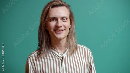Portrait of handsome young man with long hair smiling at camera isolated over green background
