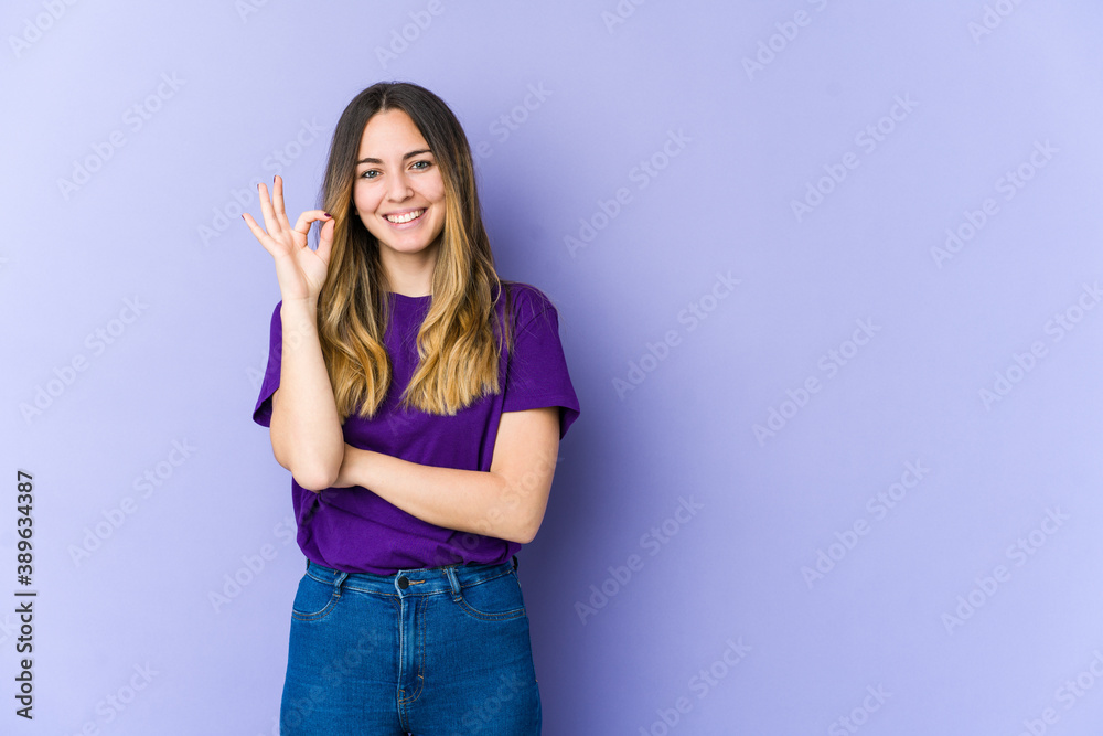 Young caucasian woman isolated on purple background winks an eye and holds an okay gesture with hand. Young caucasian woman isolated on purple background winks an eye and holds an okay gesture with hand.