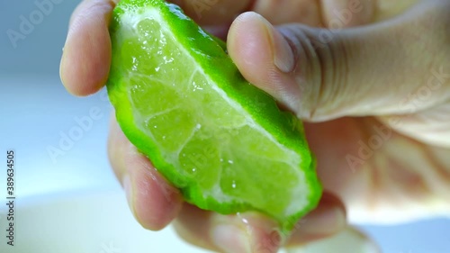 Female hand squeezing half of bergamot on blur background.