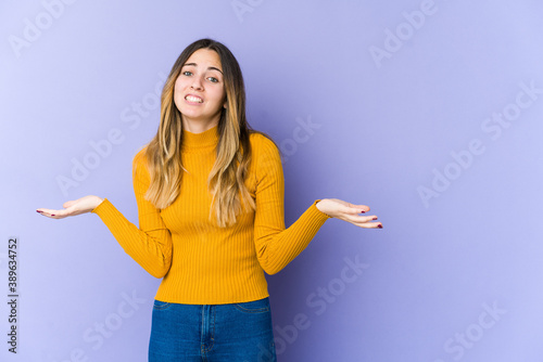 Young caucasian woman isolated on purple background confused and doubtful shrugging shoulders to hold a copy space.