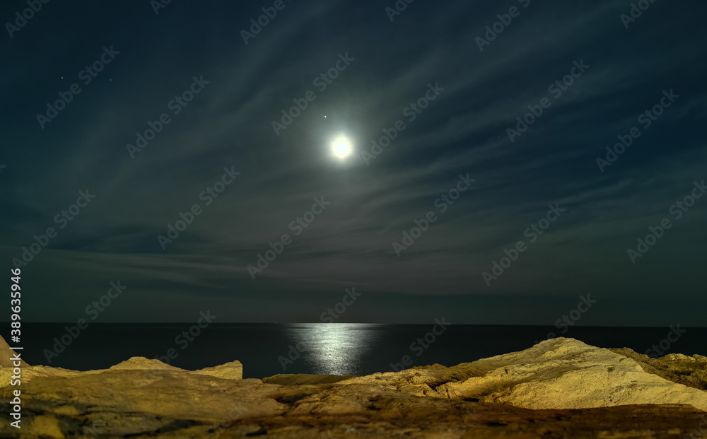 Obraz premium bsh Luna tra le nuvole sul mare di sera vista dagli scogli con riflessi di luce sull’acqua in inverno