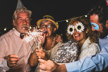 group of people having fun and enjoying new year night together celebrating with sparklers and funny accessories - happy lifestyle