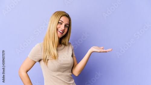 Young blonde caucasian woman showing a copy space on a palm and holding another hand on waist. © Asier