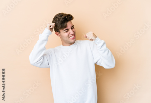 Young caucasian man isolated on beige background raising fist after a victory, winner concept.