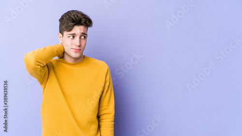 Young caucasian man isolated on purple background touching back of head, thinking and making a choice.