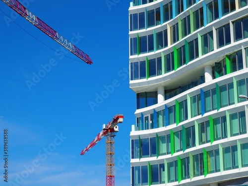Modern building with blue and green colour windows construction detail and red colour tower cranes in front of blue sky in Budapest, Hungary