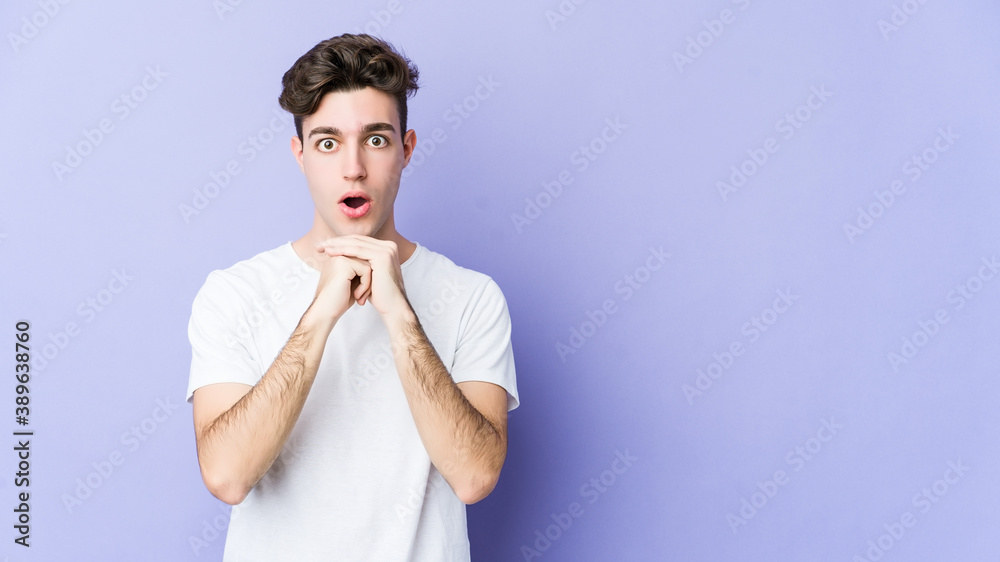 Young caucasian man isolated on purple background praying for luck, amazed and opening mouth looking to front.