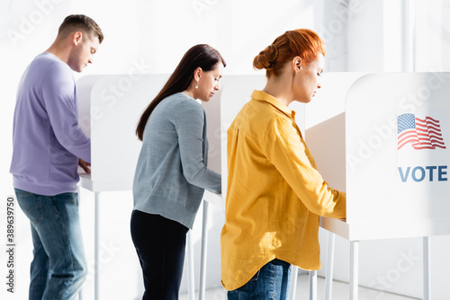 electors in polling booths with american flag and vote lettering on blurred background
