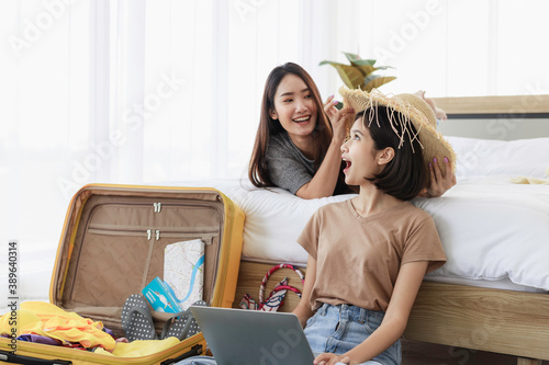 Two young asian women are using laptop to plan travel, book tickets, and booking accommodation online in bedroom. concept of travel in summer and holiday.