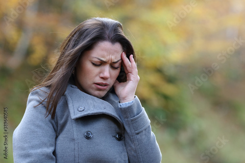 Stressed woman suffering migraine in a park in winter