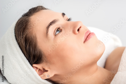 Side view portrait of pensive young woman lying on beautician table while waiting for cosmetic procedure in beauty salon
