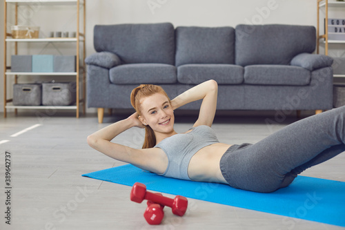 Smiling girl lying on fitness carpet, doing workout and looking at camera at home
