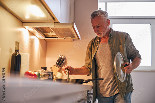 Fotografie Senior gentleman lifting the lid off frying pan on cooker