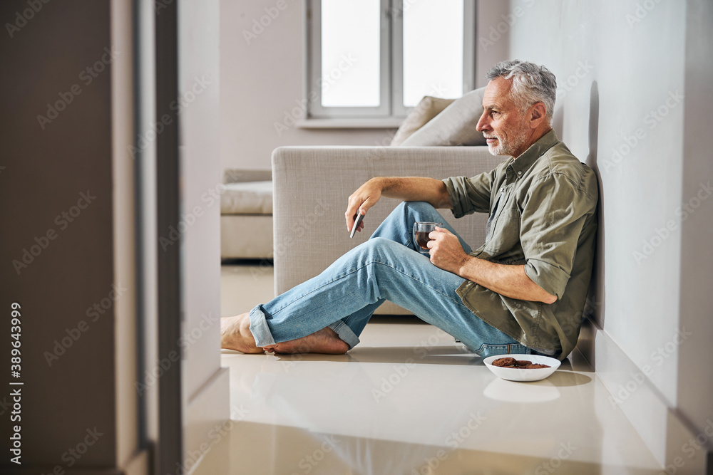 Grey-haired gentleman having tea with cookies on the floor