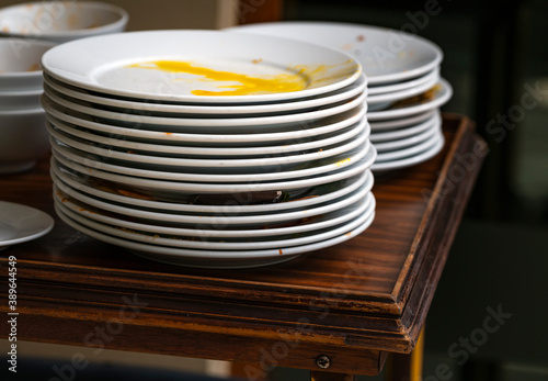 Used white food plates stacked in layers, food residue in the dish. Food plate on wooden table, waiting to clean.