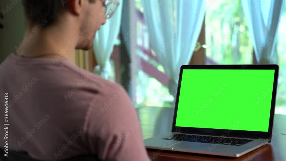 Over the shoulder shot of man having video chat working on laptop with green screen display with friends, family, work. Over the shoulder shot of man having video chat working on laptop with green screen display with friends, family, work.