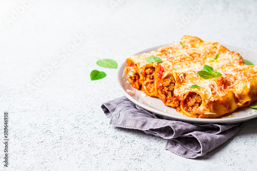 Portion of cannelloni with meat, tomato sauce and cheese on gray plate, gray background. Italian cuisine concept. photo
