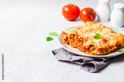 Portion of cannelloni with meat, tomato sauce and cheese on gray plate, gray background. Italian cuisine concept. photo