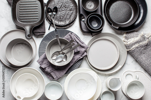 Flat lay of empty clean black, gray and white plates and bowls on white marble background. Cooking background.