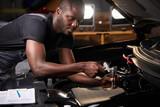 african professional auto service technician in uniform standing near car hood repairing and using check list for car inspect, indoors