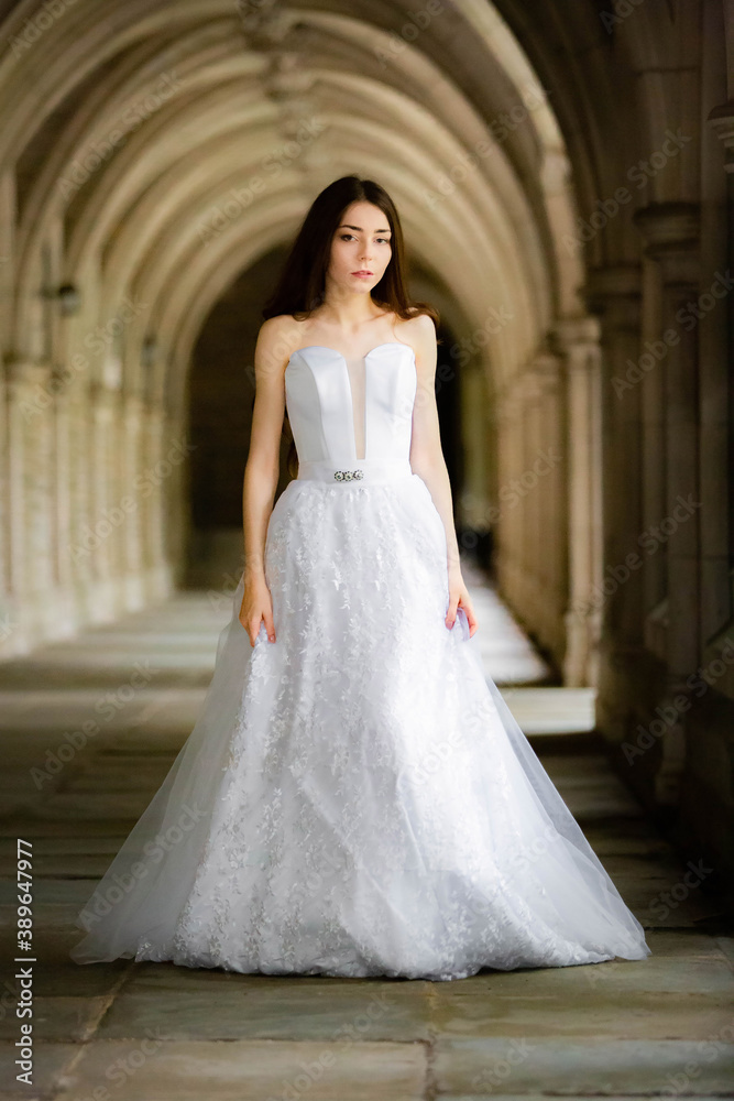 Beautiful girl wearing white wedding dress posing alone at a castle hall