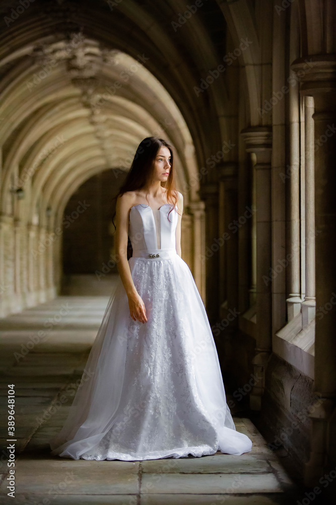 Beautiful girl wearing white wedding dress posing alone at a castle hall Beautiful girl wearing white wedding dress posing alone at a castle hall
