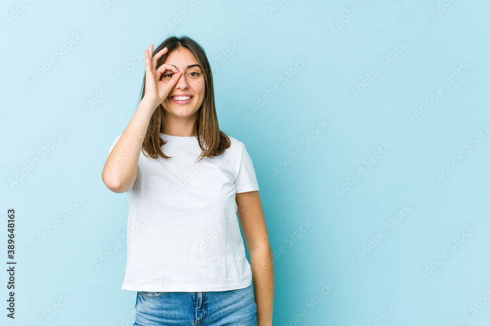 Young caucasian woman excited keeping ok gesture on eye. Young caucasian woman excited keeping ok gesture on eye.