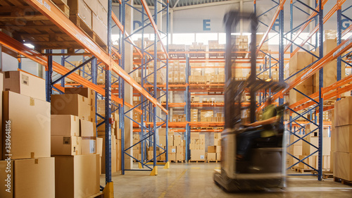 Bild auf Leinwand In Warehouse Shot of Blurred Forklift Driving with Pallets Moving Cardboard Boxes with Products from Shelves