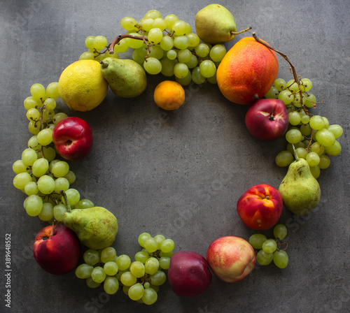 Summer fruit composition. Colorful grapes  nectarines  mango and pears wreath top view photo. Dark grey textured background with copy space. 