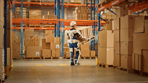 High-Tech Futuristic Warehouse: Worker Wearing Advanced Full Body Powered exoskeleton, Walks with Heavy Pallet full of Cardboard Boxes. Delivery Exosuit amplifies strength.