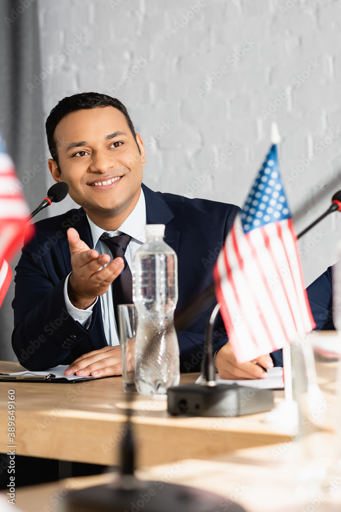 Obraz premium Smiling indian politician pointing with hand, while looking away, sitting near colleague on blurred foreground