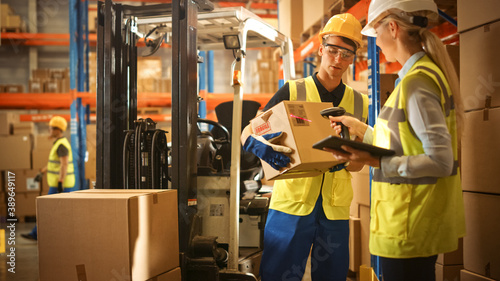In Warehouse Manager Uses Digital Tablet and Scans Cardboard Boxes for Inventory, Talks with Forklift Driver about Package Delivery. Workers in Global Distribution Center with Shelves with Goods  photo
