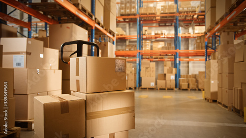 Big Retail Warehouse full of Shelves with Goods Stored on Manual Pallet Truck in Cardboard Boxes and Packages. Forklift Driving in Background. Logistics and Distribution Facility for Product Delivery