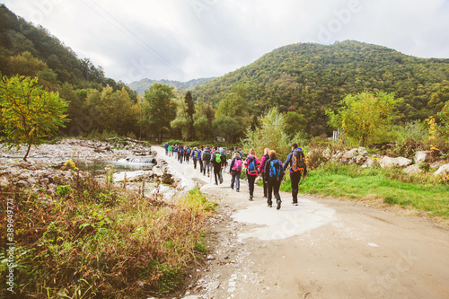 Group of active people hiking on autumn day through beautiful nature landscape. Real unrecognizable hikers, rearview, cloudy sky in the background.