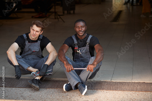 two auto mechnic colleagues take a break during work, sit on the floor resting photo