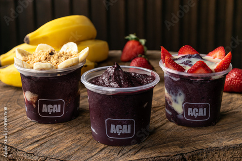 Mix of Delicious Brazilian Açaí Cream, in a plastic Cup With a variety of Toppings, in a rustic wooden background. Summer acai smoothie