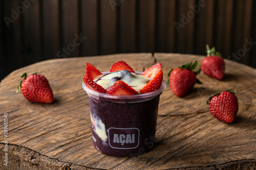 Delicious Brazilian Açaí Cream, in a plastic Cup With Strawberry Topping, in a rustic wooden background. Summer acai smoothie