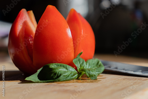 Fresh cut tomato on the cutting desk with knife and leave of the basil. 