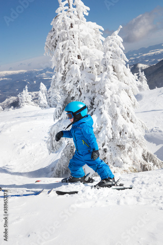 toddler boy in helmet, goggles and blue overalls skiing in beautiful snowy mountains. Winter active entertainment for children. Skiing lesson at an alpine school. Cold, sunny, beautiful