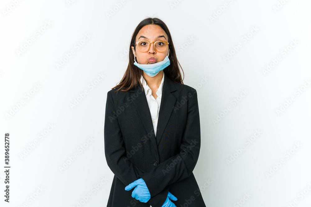 Young business latin woman wearing a mask to protect from covid isolated on white background blows cheeks, has tired expression. Facial expression concept. Young business latin woman wearing a mask to protect from covid isolated on white background blows cheeks, has tired expression. Facial expression concept.