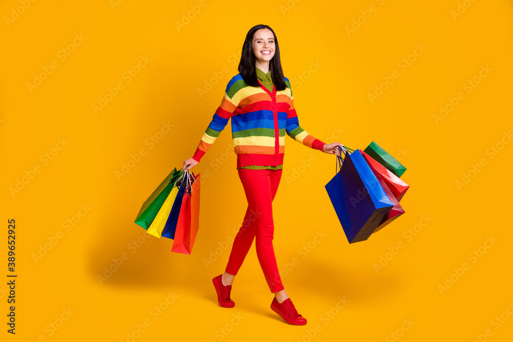 Full body photo of young cheerful girl carry shopping bags smile enjoy go walk isolated over yellow color background Full body photo of young cheerful girl carry shopping bags smile enjoy go walk isolated over yellow color background