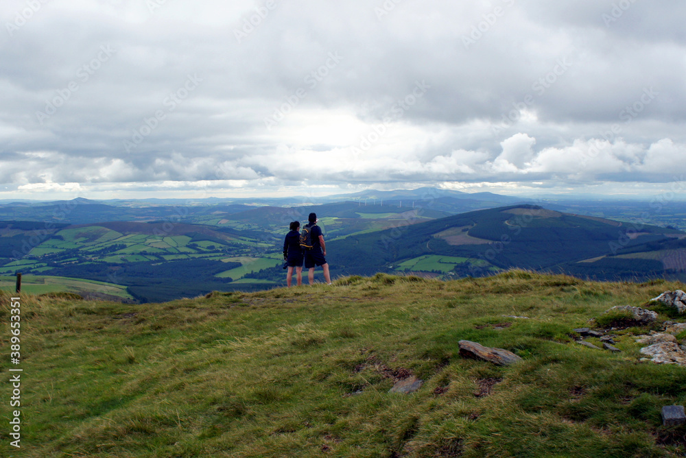 A couple of tourists on the top of the mountain under a cloudy sky.