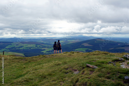 A couple of tourists on the top of the mountain under a cloudy sky.