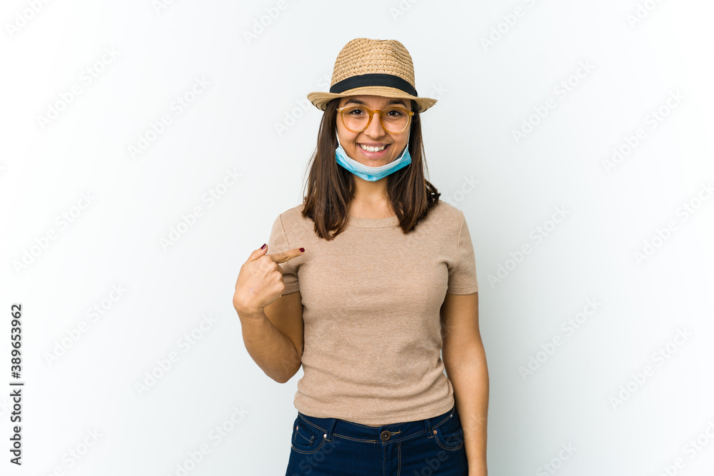 Young latin woman wearing hat and mask to protect from covid isolated on white background person pointing by hand to a shirt copy space, proud and confident