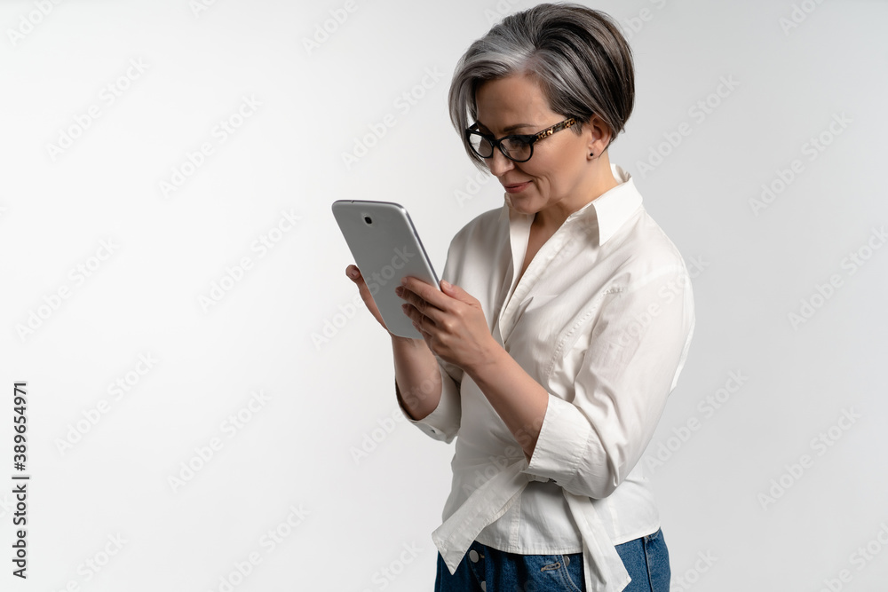 Focused mature woman works on a tablet while standing on white background. High quality photo Focused mature woman works on a tablet while standing on white background. High quality photo