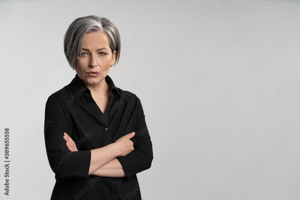 Mature woman with gray hair In black shirt folded her arms on her chest against a white background. copy space at right. High quality photo. Mature woman with gray hair In black shirt folded her arms on her chest against a white background. copy space at right. High quality photo.
