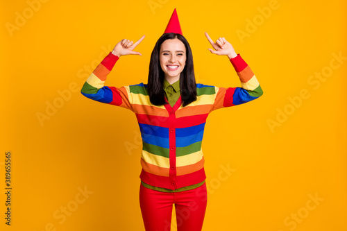 Photo of young positive girl wear party hat celebrate show point fingers up isolated over yellow color background