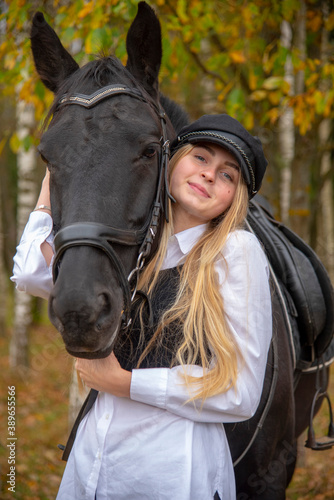  portrait of a girl with blonde hair , wearing a cap, and a Bay horse on the background of a forest. 